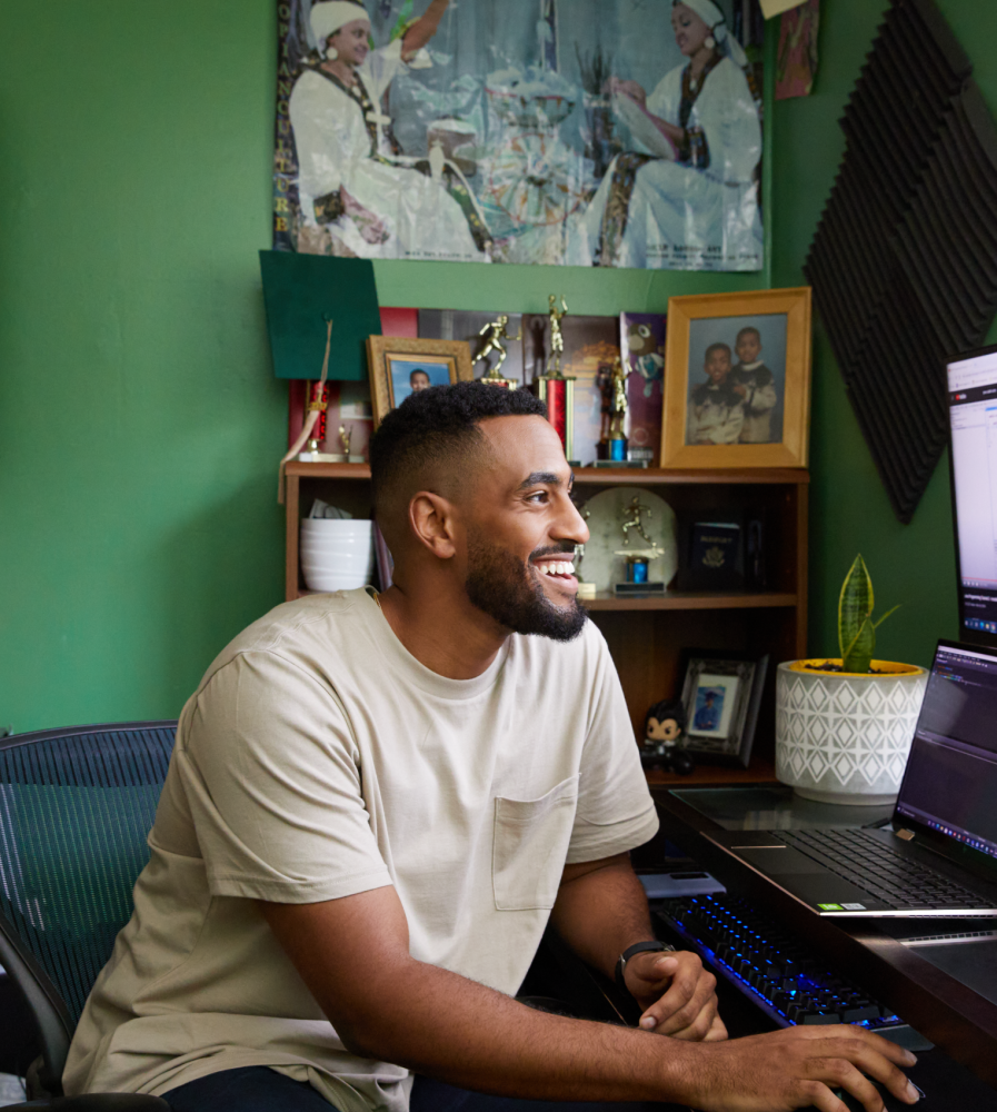 A man smiles as he scrolls on his computer at his desk.